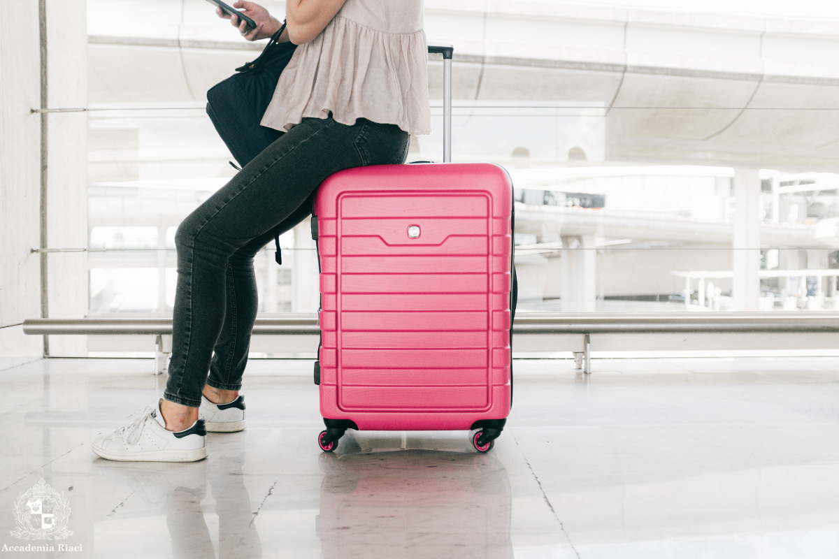 空港で使うイタリア語　空港でピンク色のスーツケースに腰掛けている女性